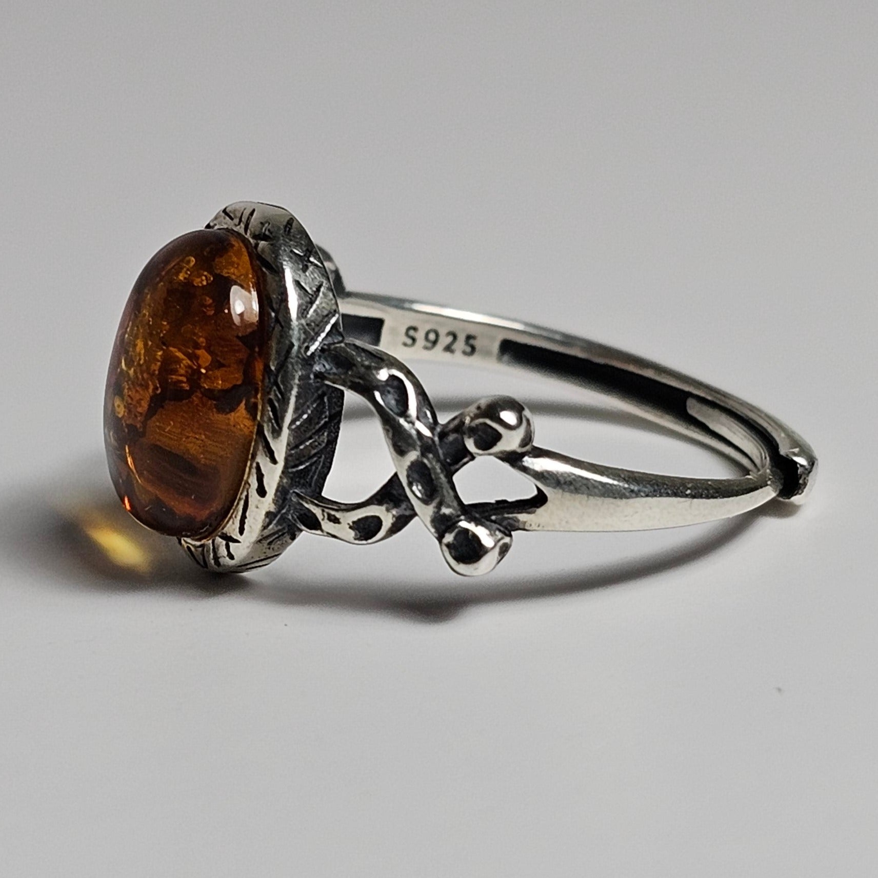 This adjustable ring is crafted from sterling silver and features a beautiful oval shaped Amber stone with a textured bezel and criss-cross designed shoulders.