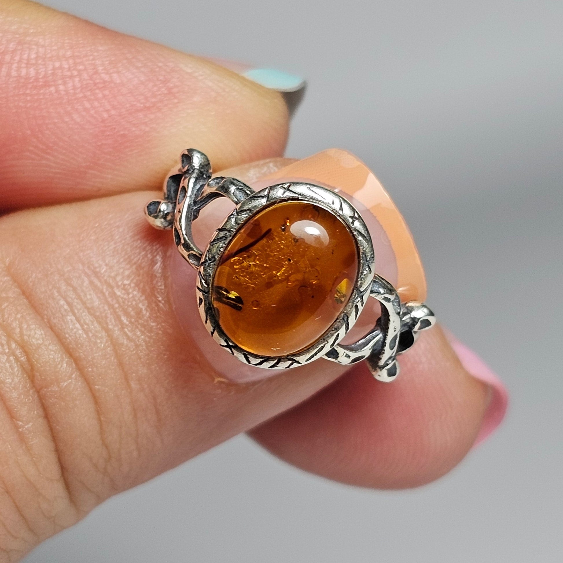 This adjustable ring is crafted from sterling silver and features a beautiful oval shaped Amber stone with a textured bezel and criss-cross designed shoulders.