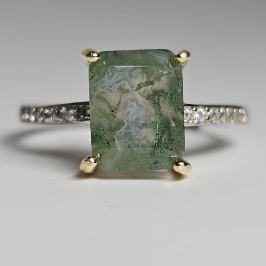 This adjustable ring is crafted from sterling silver and features a stunning rectangular Moss Agate centre stone on gold plated prongs, with zircons on the shoulders of the ring band.