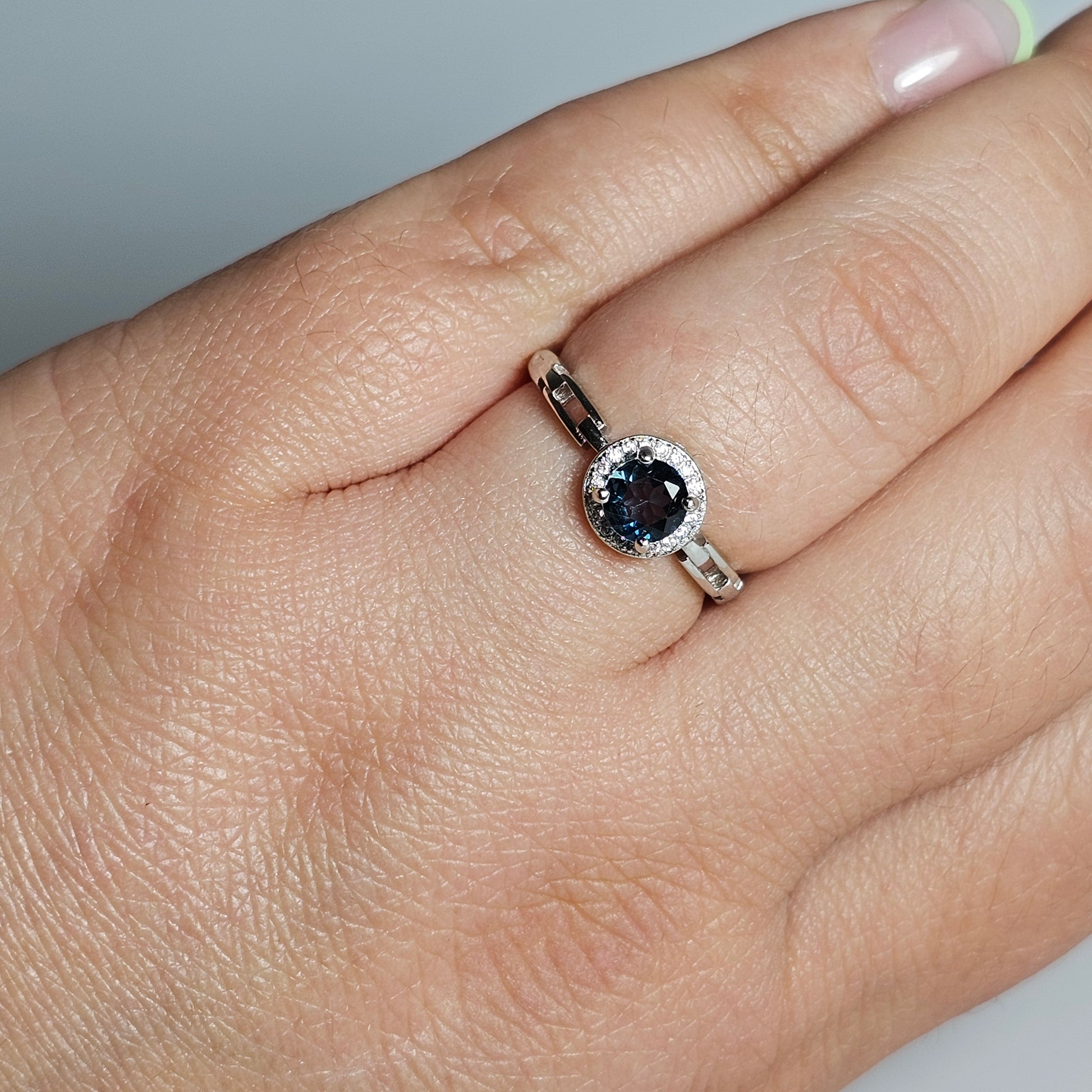 This adjustable ring is crafted from sterling silver and features a gorgeous round London Blue Topaz centre stone on a zircon prong setting crown, with link accented shoulder ring band.