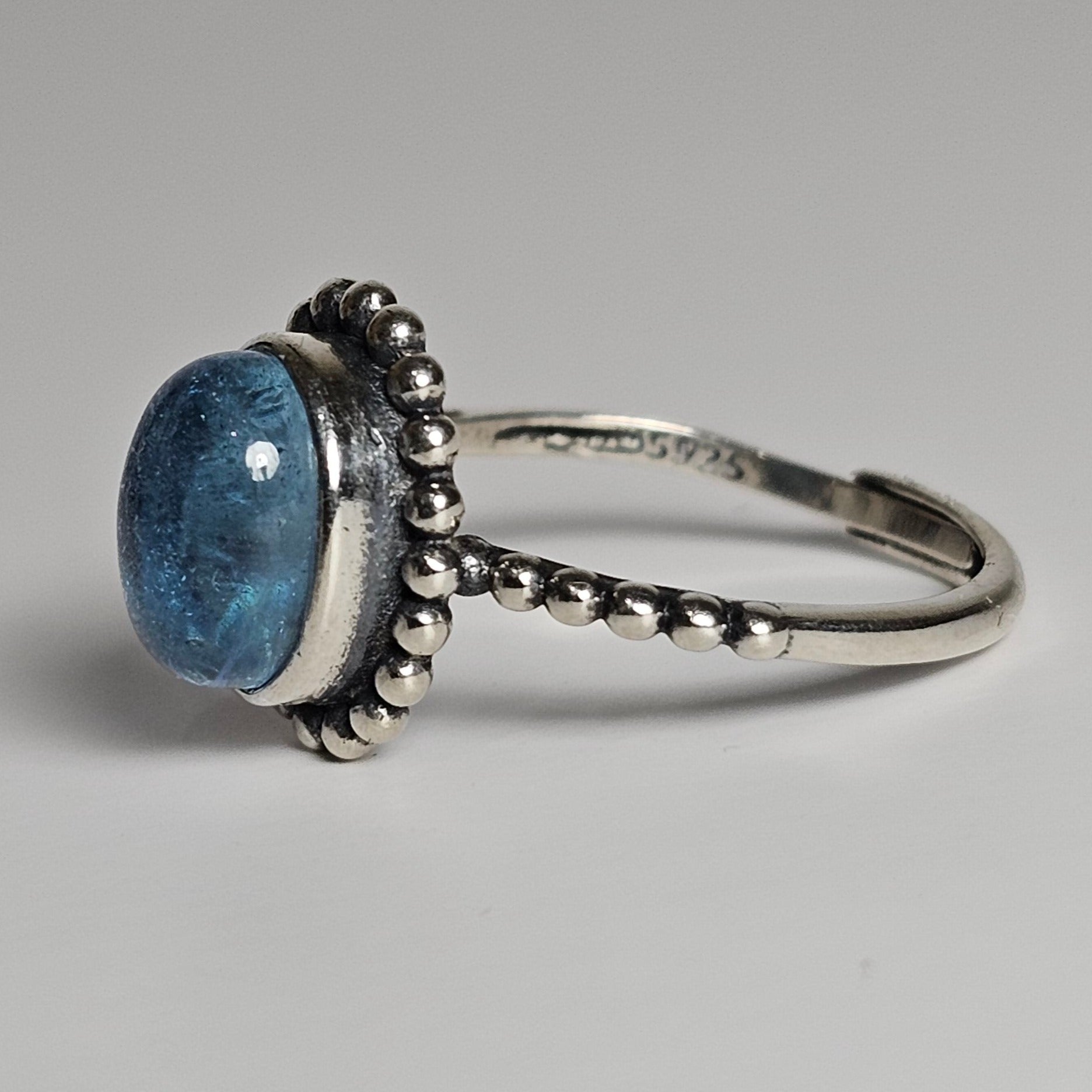 This adjustable ring is crafted from sterling silver and features a gorgeous oval Aquamarine stone on a beaded bezel, and beaded shoulder ring band.