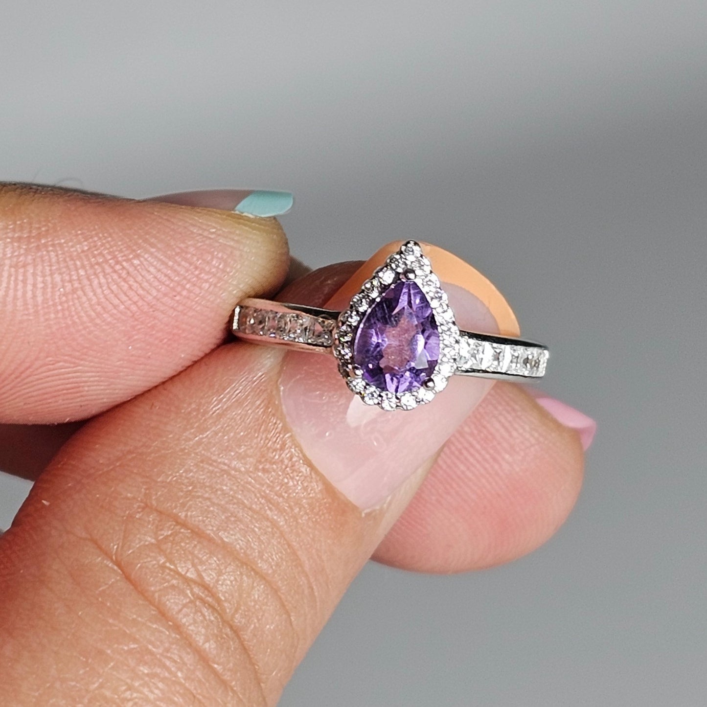 This adjustable ring is crafted from sterling silver and features a gorgeous pear shaped Amethyst centre stone with a Zircon accented crown and shoulder ring band.