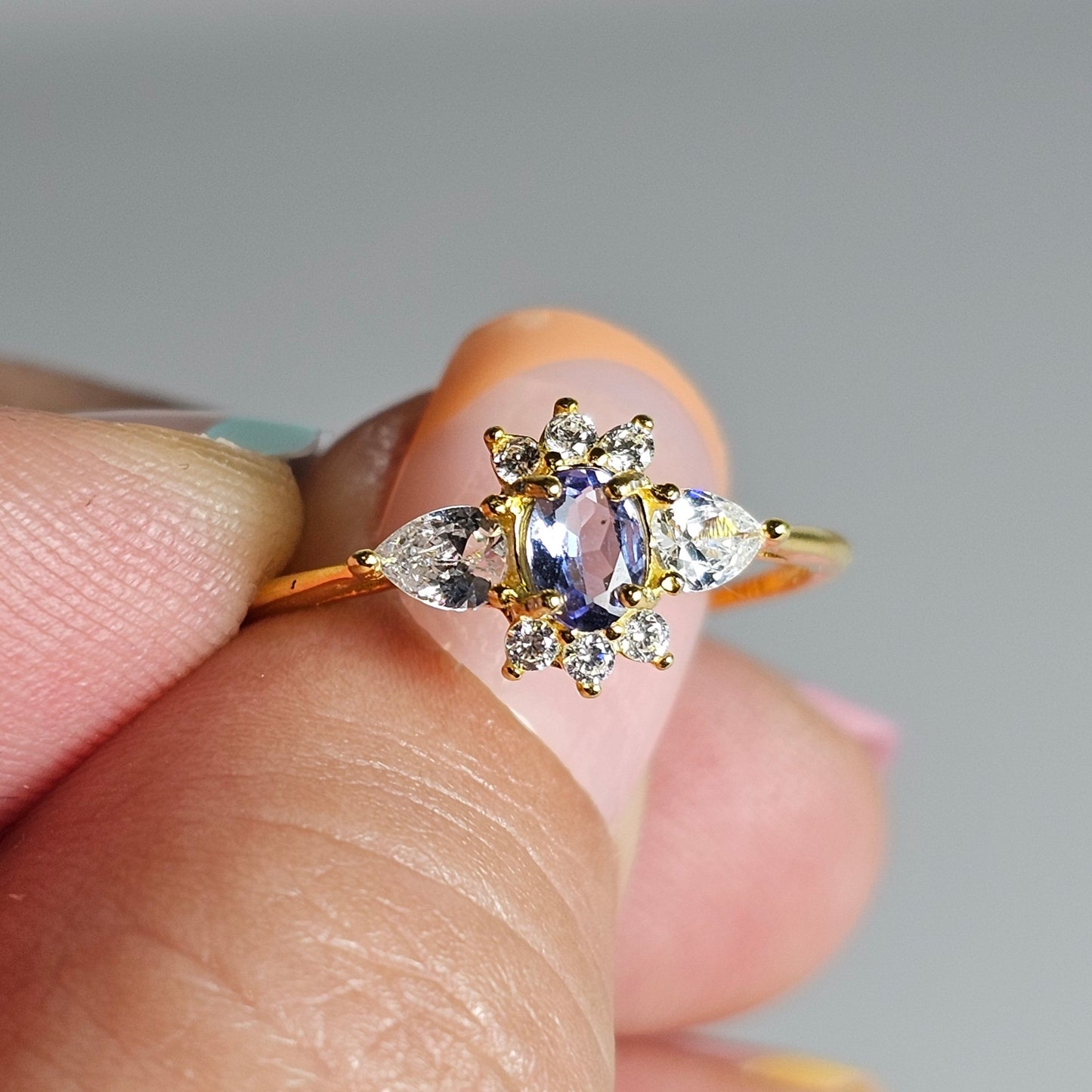 This adjustable ring is crafted from gold plated sterling silver and features a beautiful oval shaped Tanzanite centre stone surrounded with zircon.