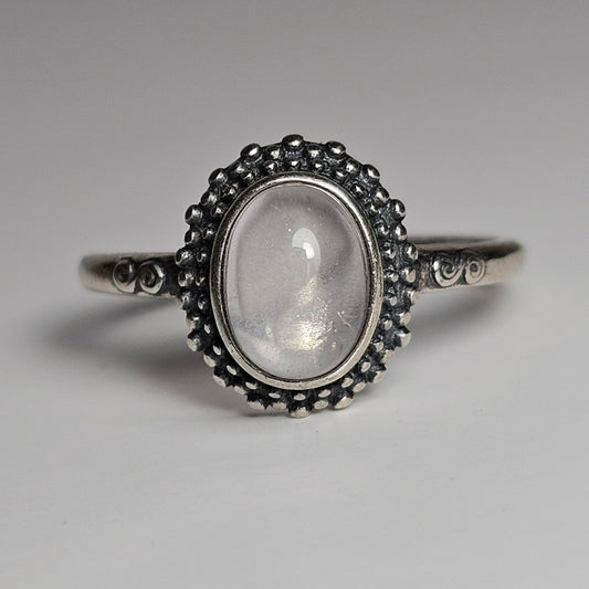 This adjustable ring is crafted from sterling silver and features an oval Star Rose Quartz stone on a beaded bezel, with swirl details on the shoulders of the ring band.