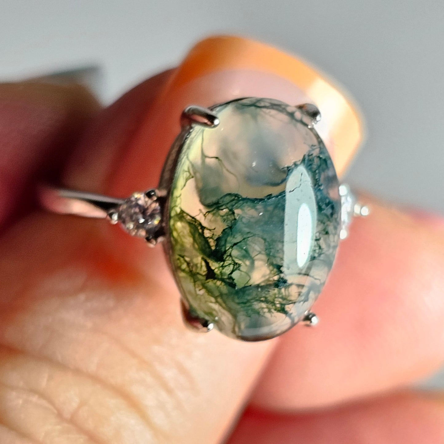 This adjustable ring is crafted from sterling silver and features a beautiful oval shaped Moss Agate with zircon side stones.