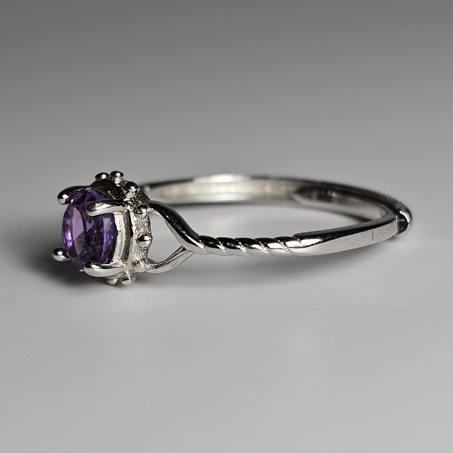This adjustable fine ring is crafted from sterling silver and features a round Amethyst with heart and twist accented shoulder ring band.
