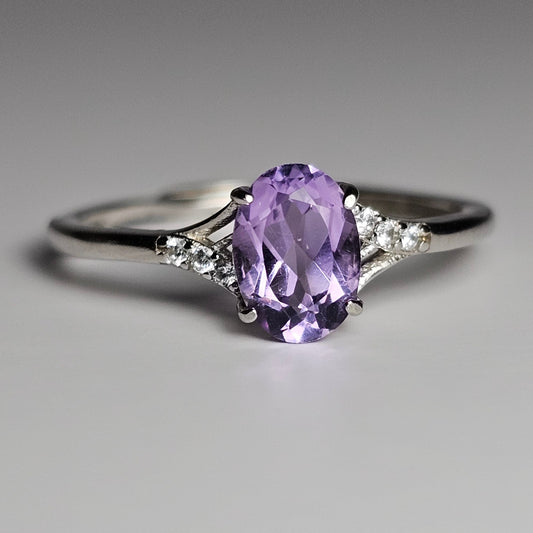 This adjustable petite ring is crafted from sterling silver and features an oval Amethyst with zircon accented shoulder ring band.