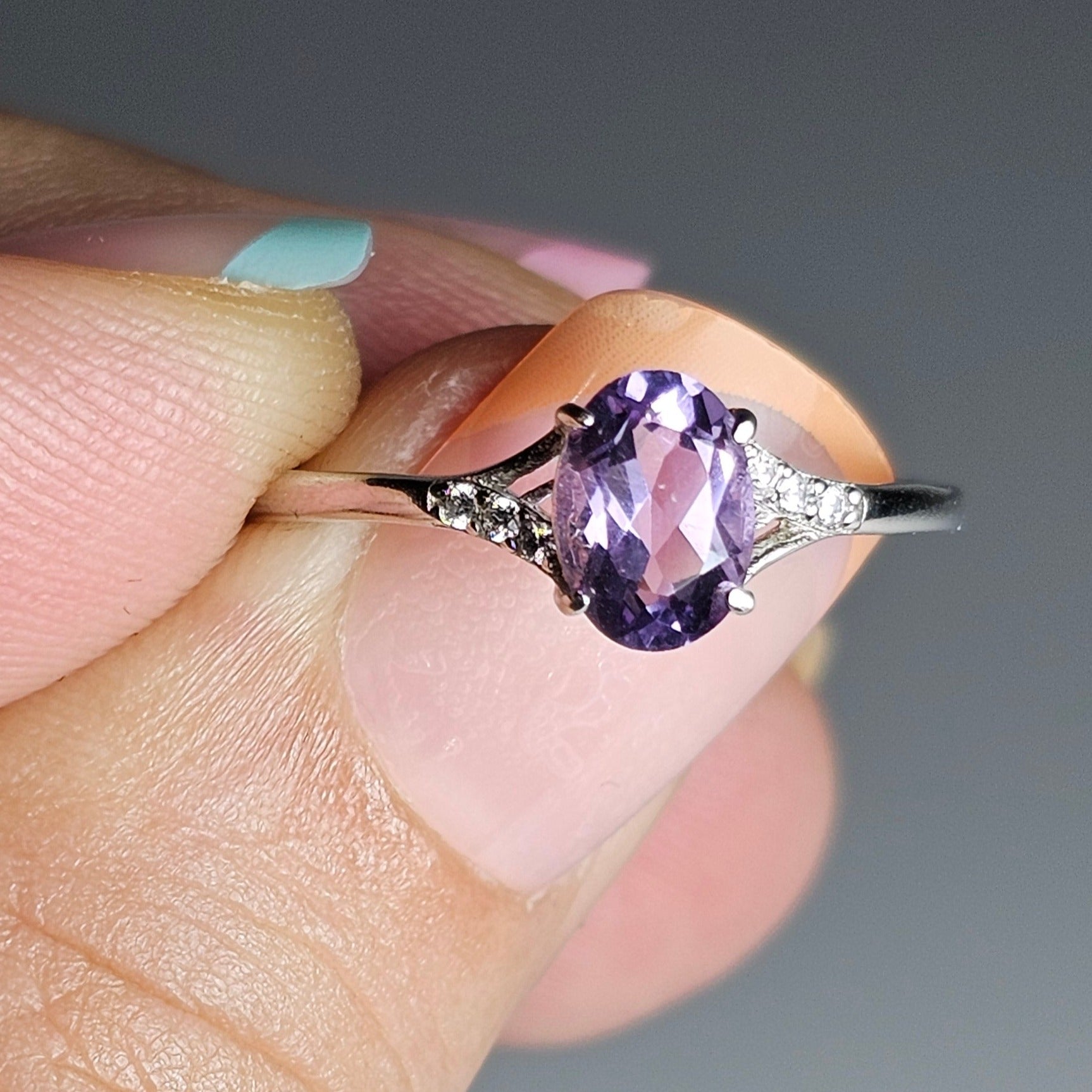 This adjustable petite ring is crafted from sterling silver and features an oval Amethyst with zircon accented shoulder ring band.