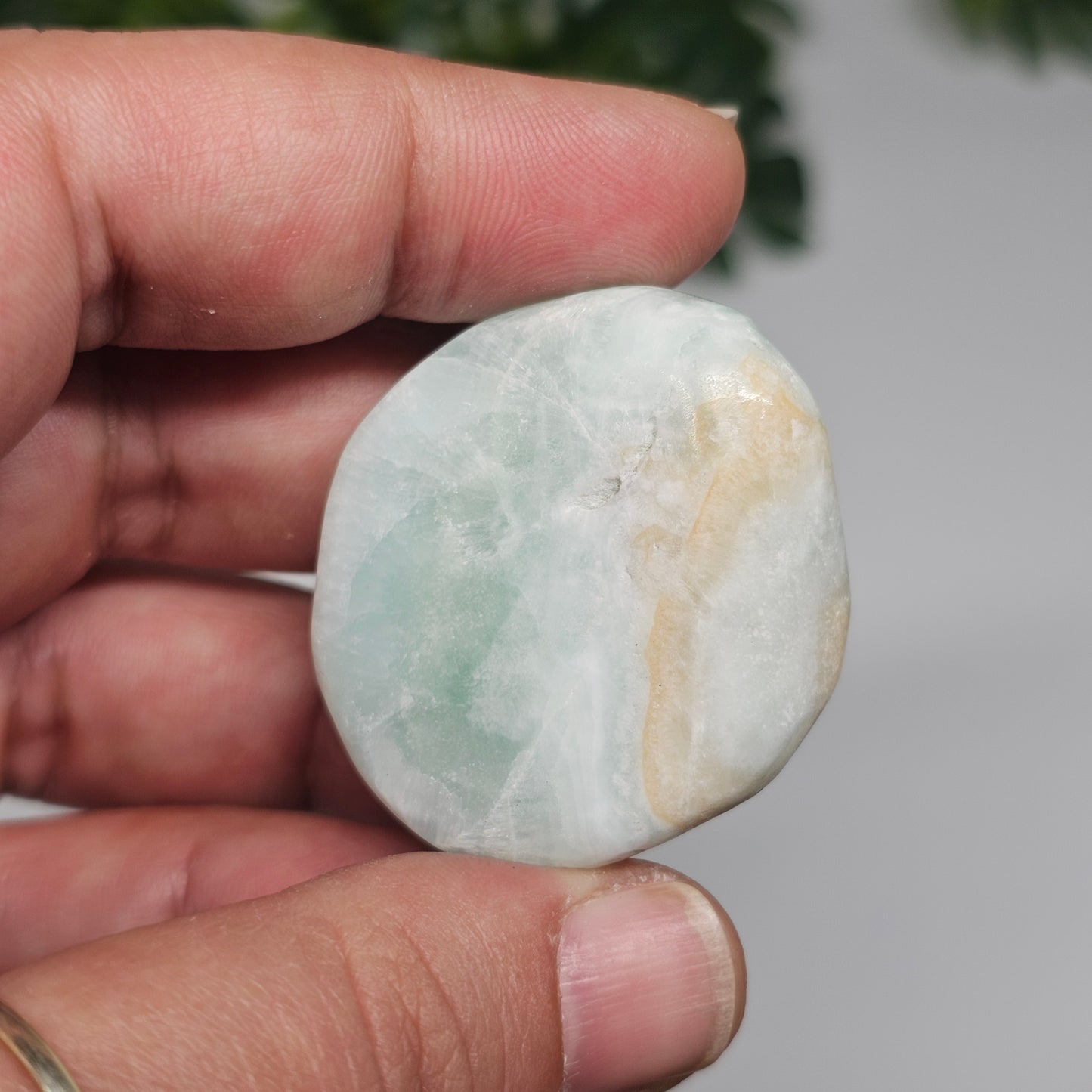 A large Caribbean Calcite tumble stone held in hand, highlighting its size, clarity, and smooth polished surface.