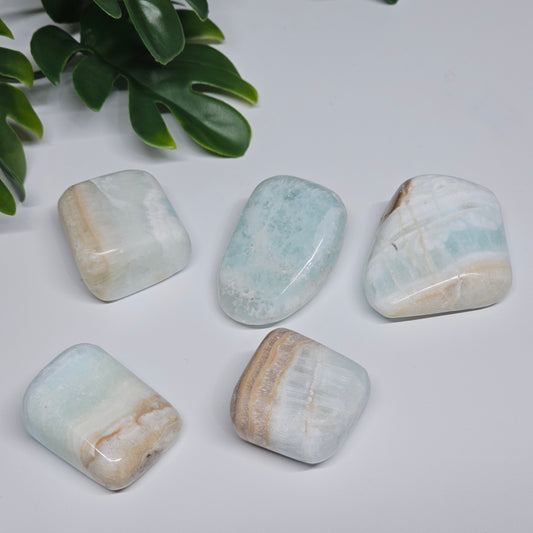 Small Caribbean Calcite tumble stones arranged on a flat surface, showcasing their soft blue tones and natural banding.