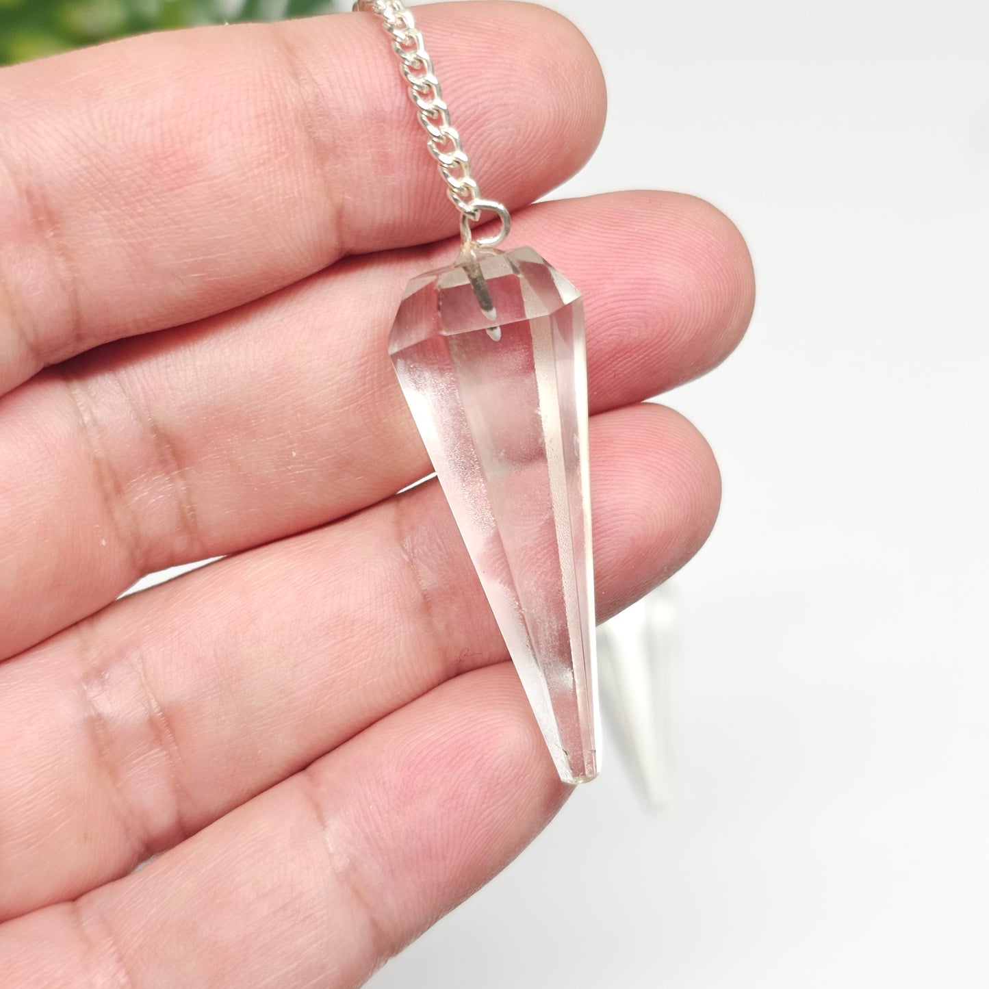 Clear Quartz pendulum held in hand to demonstrate its size, polished finish, crystal point, and chain for divination and energy work.
