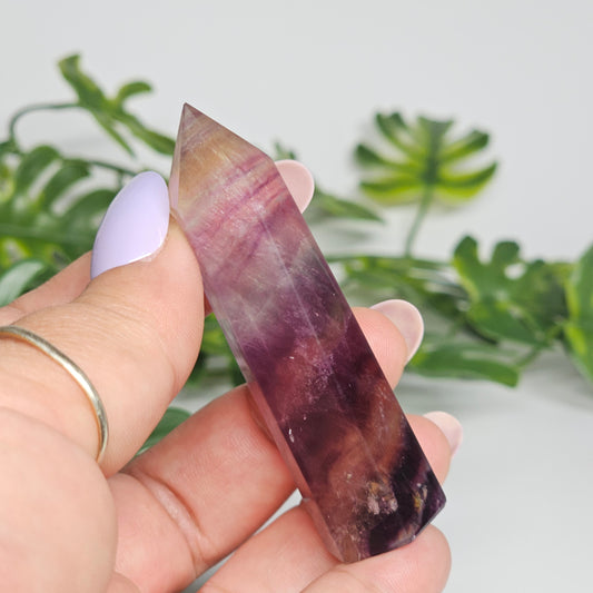 Fluorite crystal tower held in hand showing size with yellow, purple and green natural banding and polished point