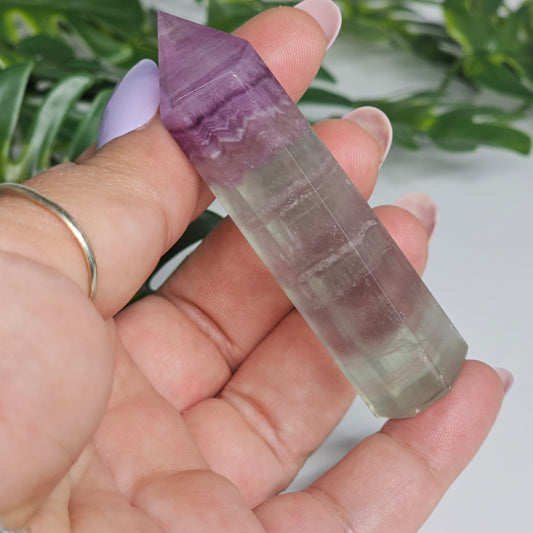Fluorite crystal tower held in hand showing size with yellow, purple and green natural banding and polished point