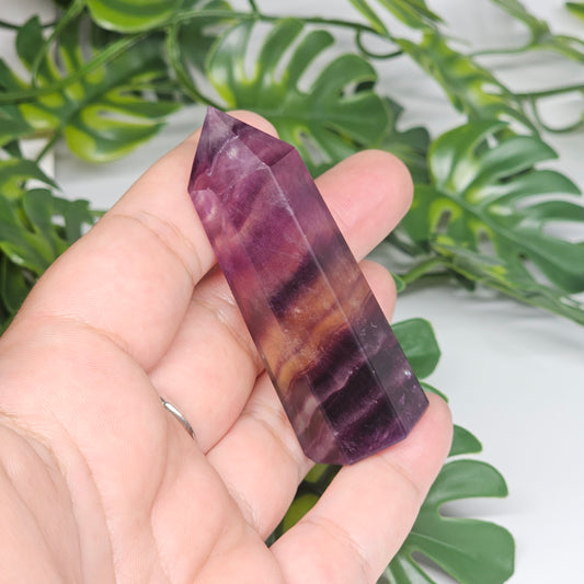Fluorite crystal tower held in hand showing size with yellow, purple and green natural banding and polished point