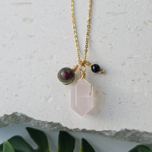 Flat lay of the Grounded Love Necklace showcasing a Rose Quartz point with Bloodstone Jasper and Black Tourmaline accents suspended from an 18k gold plated stainless steel cable chain