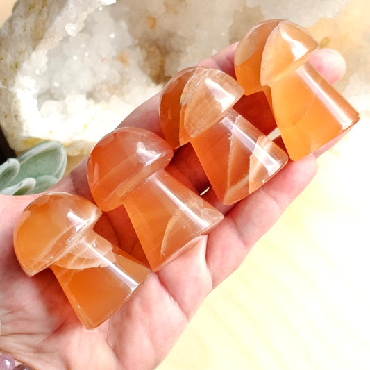 Honey Calcite mushroom carvings held in hand to show size, shape, and warm golden colouring.