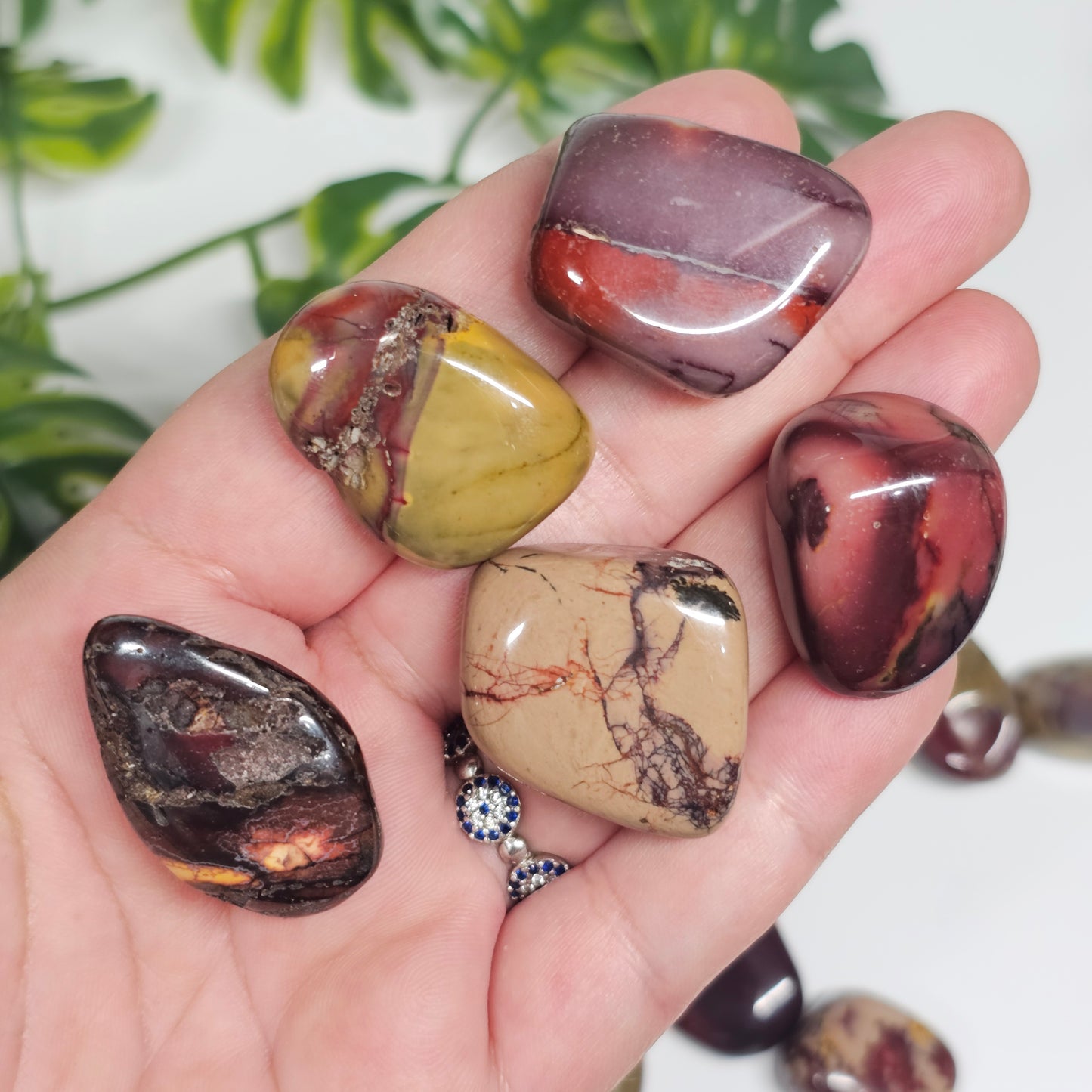 Several Mookaite Jasper tumble stones held in hand, showcasing a variety of shapes, patterns, and earthy colour variations within the collection.