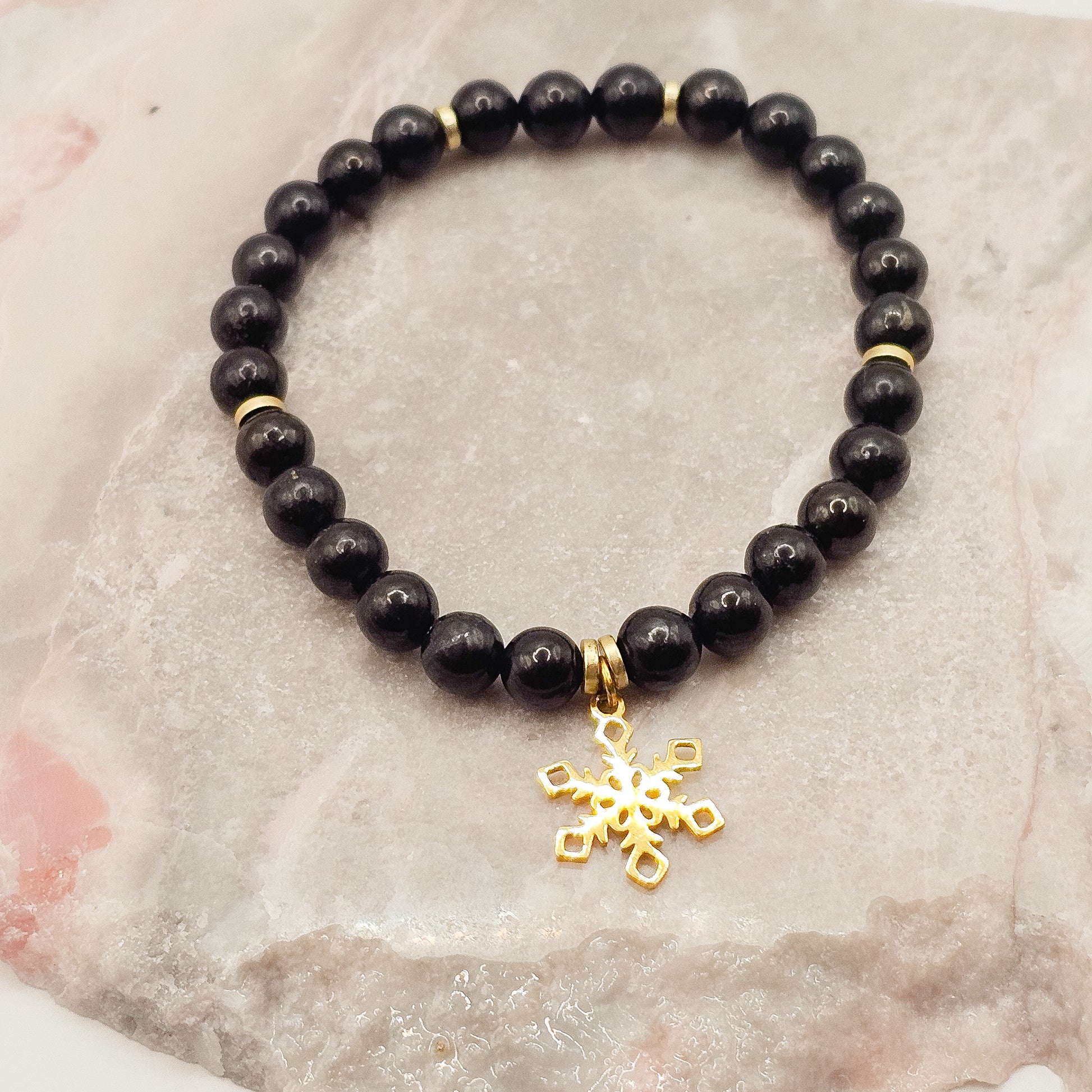 Shungite and Hematite stretch bracelet with golden stainless steel snowflake charm | When worn, Shungite is said to emit pain-killing properties and helps fight fatigue.