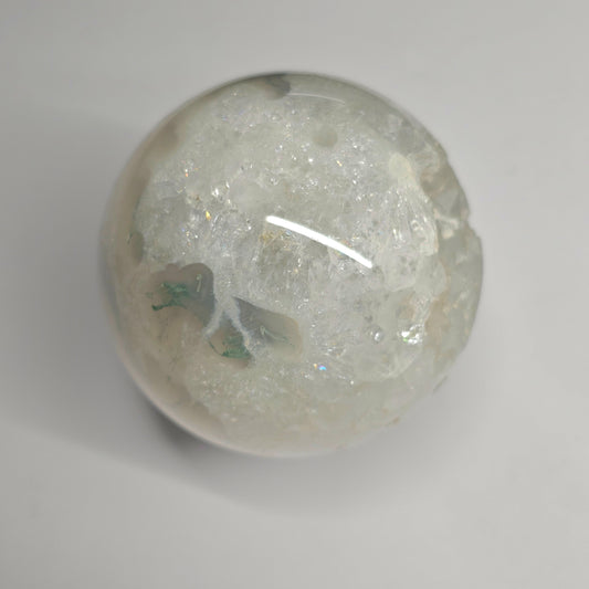 Close-up of the Moss Agate Quartz sphere highlighting natural quartz formations with mini rainbow inclusions, set within earthy green moss agate patterns and clear crystal structure.