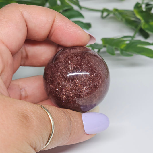 Strawberry Quartz sphere held in hand showing size, deep colouring and natural sparkle inclusions