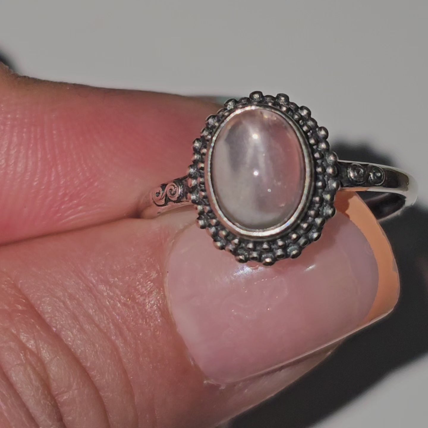 This adjustable ring is crafted from sterling silver and features an oval Star Rose Quartz stone on a beaded bezel, with swirl details on the shoulders of the ring band.