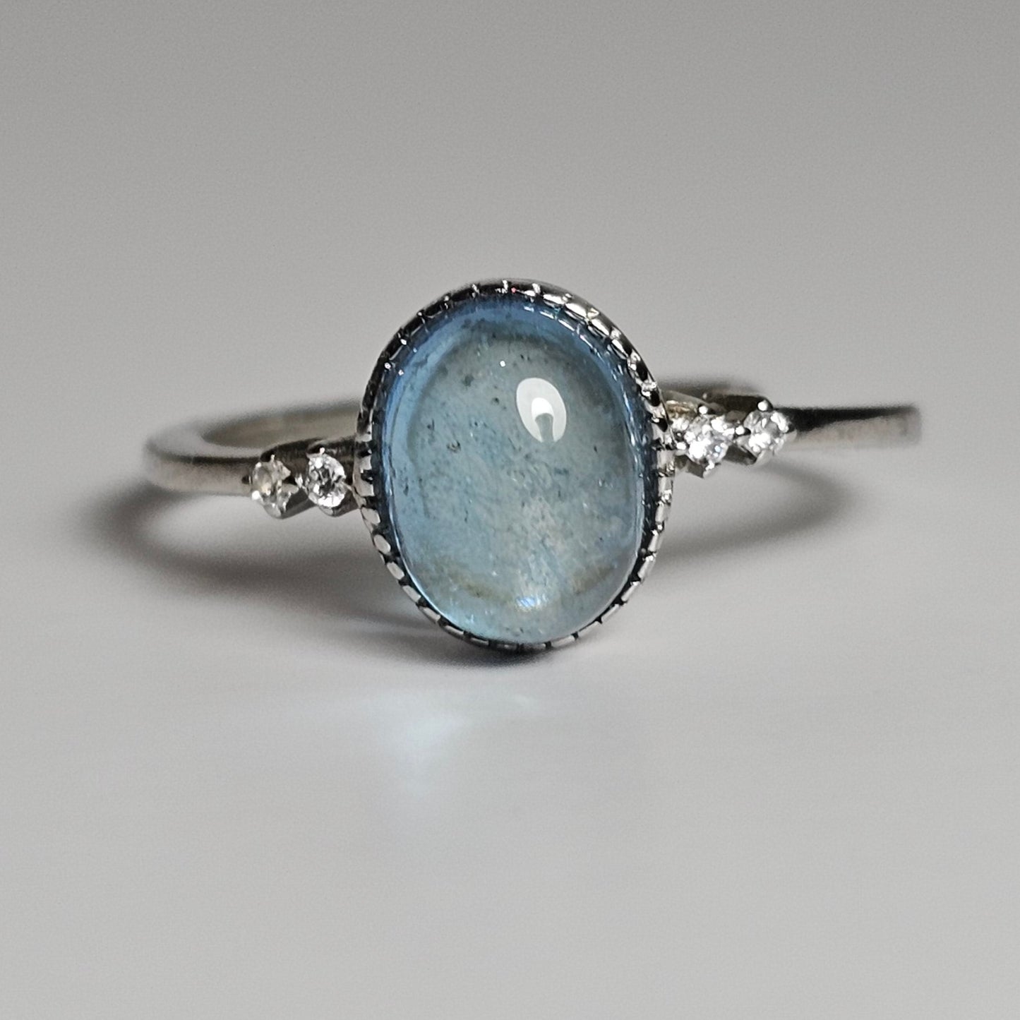 This adjustable ring is crafted from sterling silver and features a gorgeous oval Aquamarine with a Zircon accented shoulder ring band.