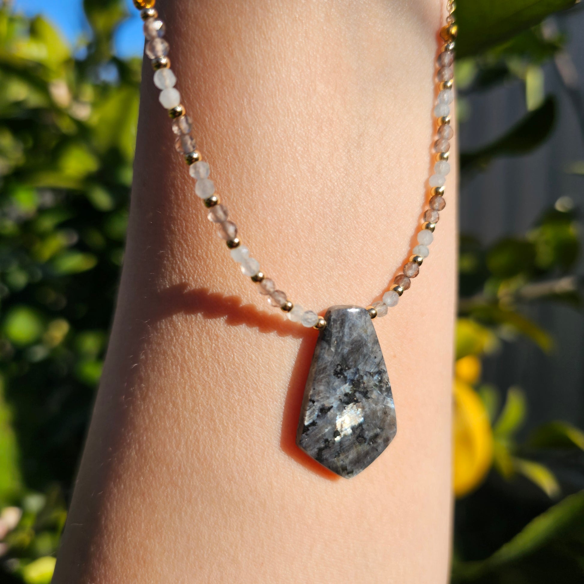 Lunar bloom is a focal Larvikite pendant necklace adorned with Smoky Quartz and Aquamarine beads.