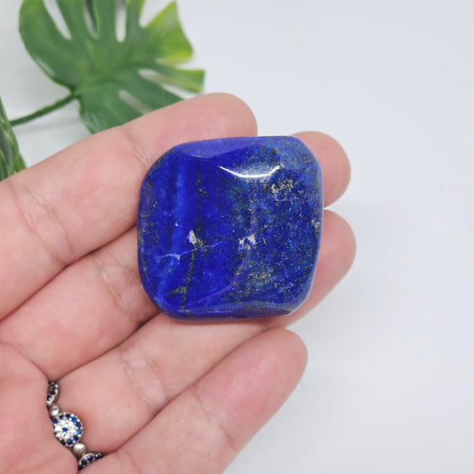 Close-up of an AA Grade Lapis Lazuli polished tumble stone held in hand, displaying deep royal blue colouring with natural golden Pyrite speckles. Premium quality crystal available in Australia.