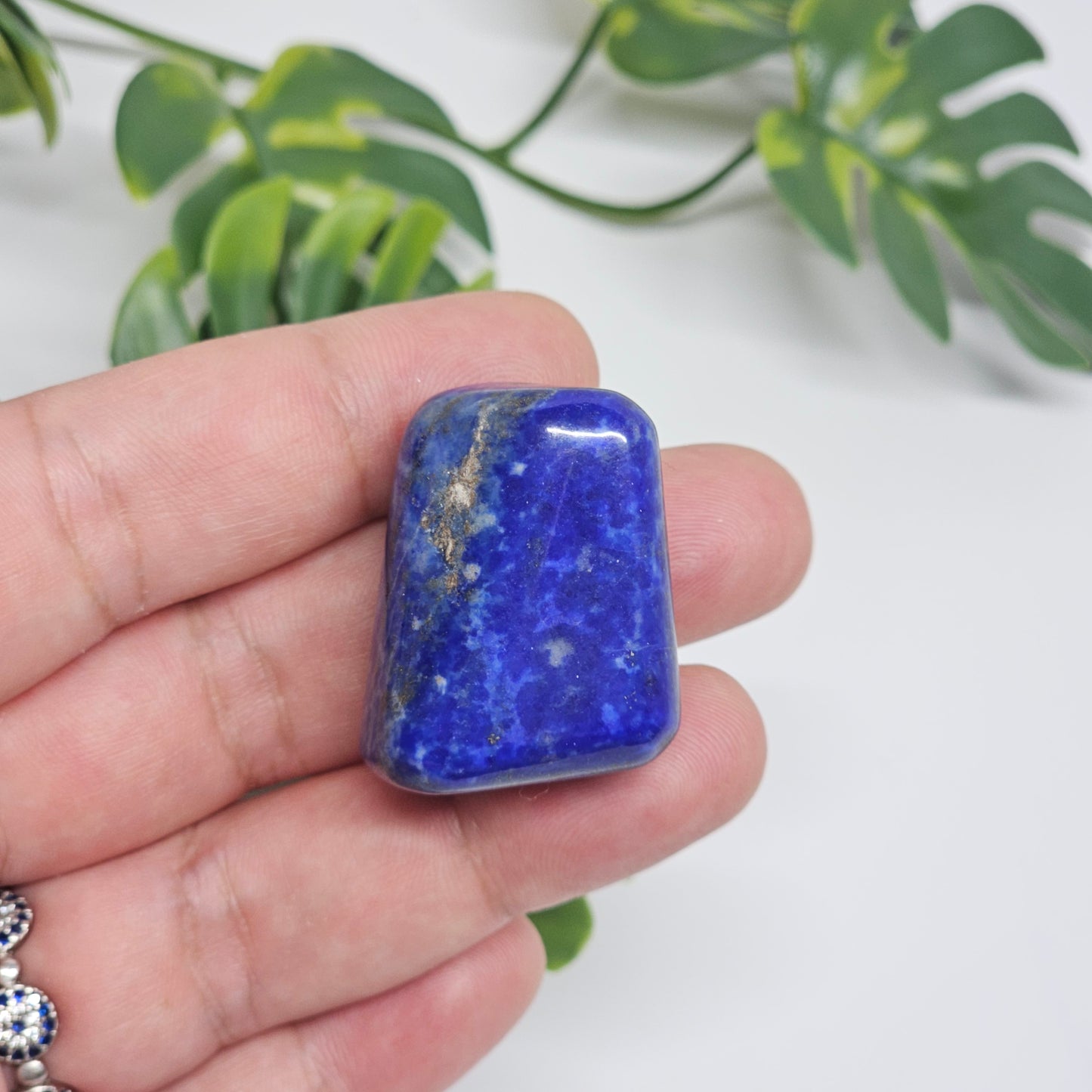 Close-up of an AA Grade Lapis Lazuli polished tumble stone held in hand, displaying deep royal blue colouring with natural golden Pyrite speckles. Premium quality crystal available in Australia.