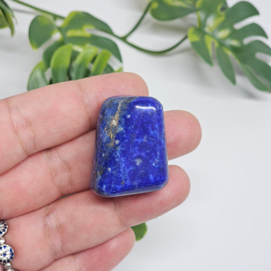 Close-up of an AA Grade Lapis Lazuli polished tumble stone held in hand, displaying deep royal blue colouring with natural golden Pyrite speckles. Premium quality crystal available in Australia.