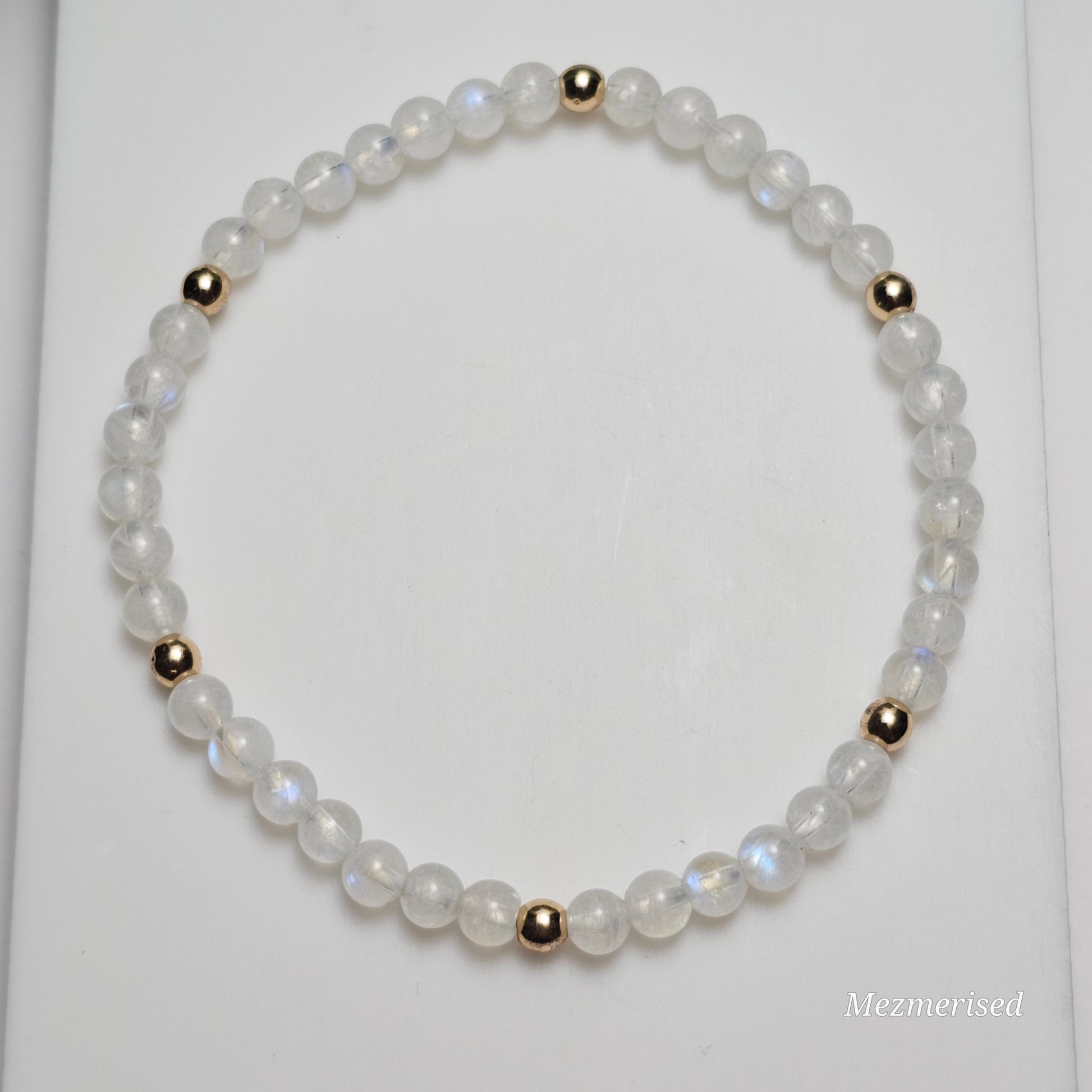 Minimal 4mm AA Grade Rainbow Moonstone bracelet with gold accents styled in flat lay display.