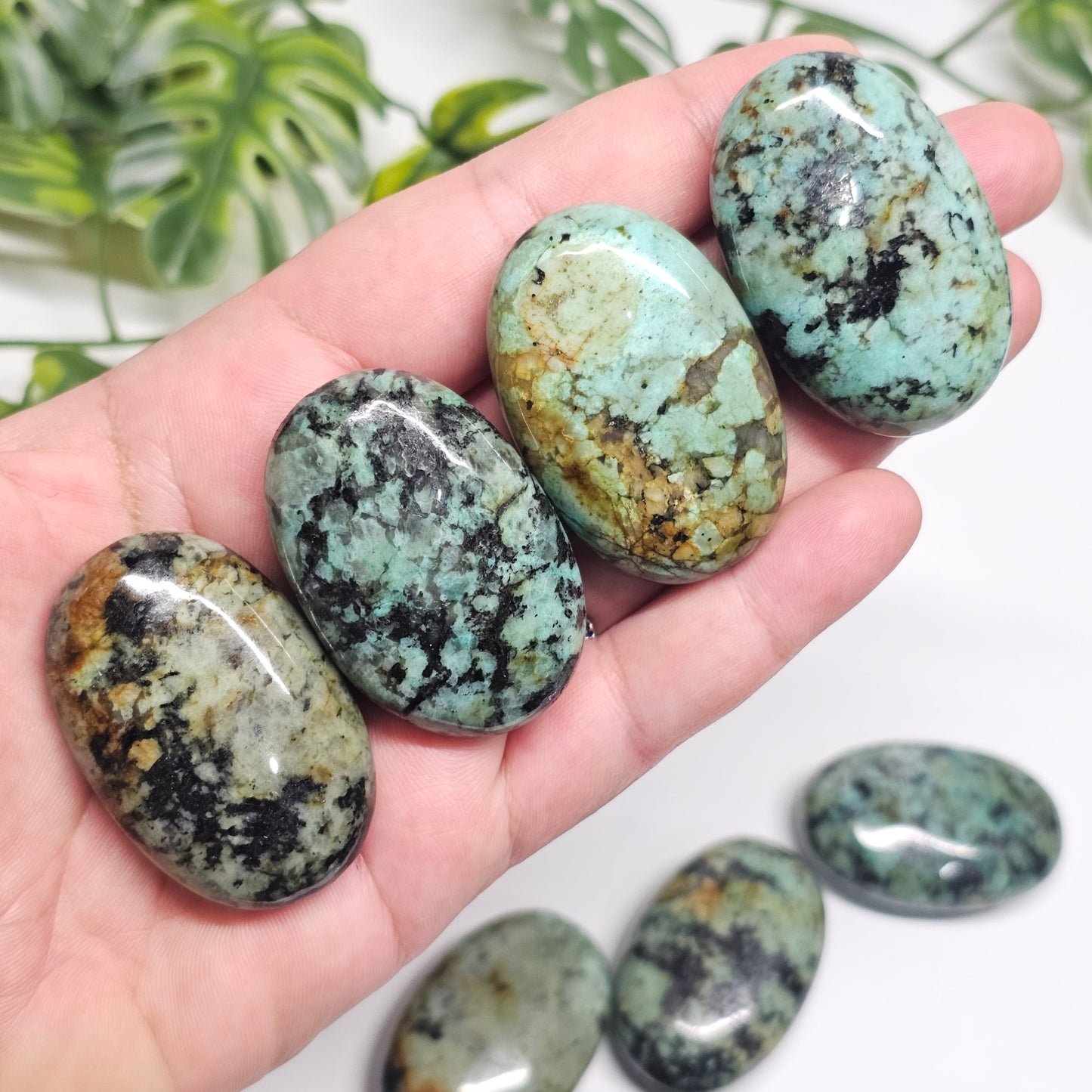 Polished African Turquoise palm stones displayed in hand, showcasing their unique green, teal, black, and earthy patterns from the front.