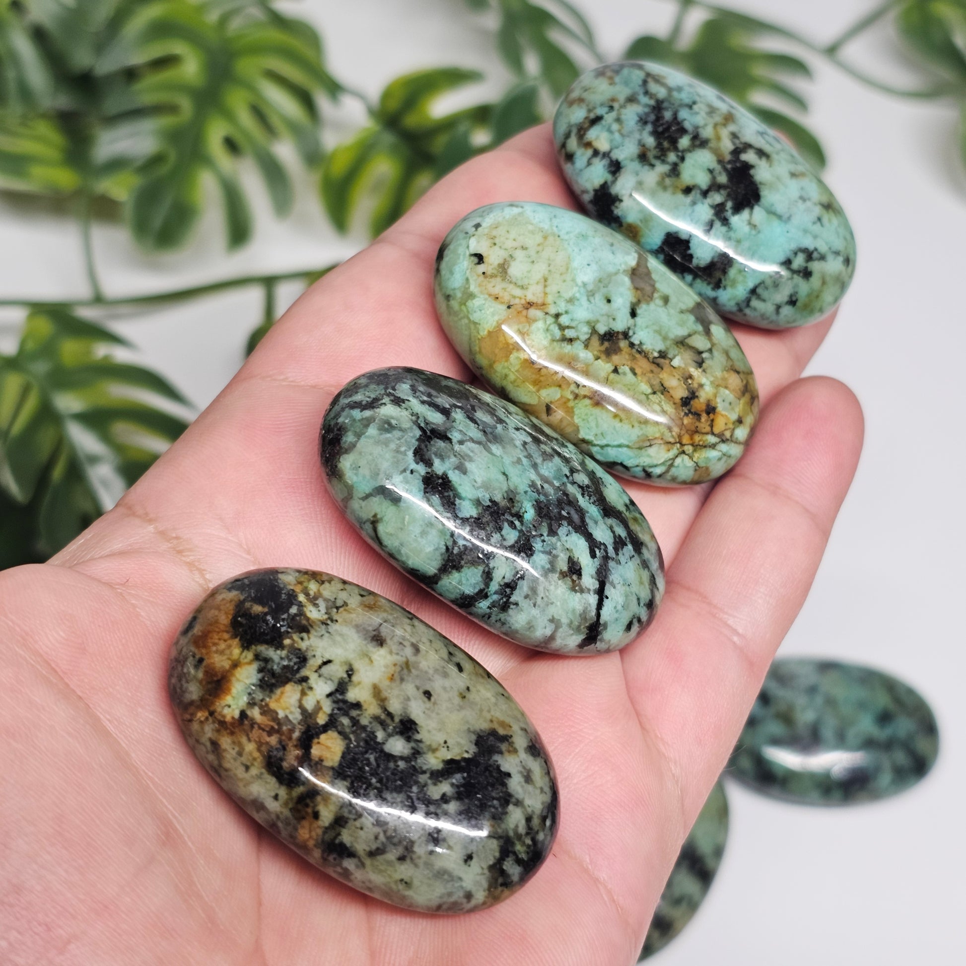 African Turquoise palm stones shown in hand from a side angle, highlighting their thickness, polished finish, and smooth palm stone shape.