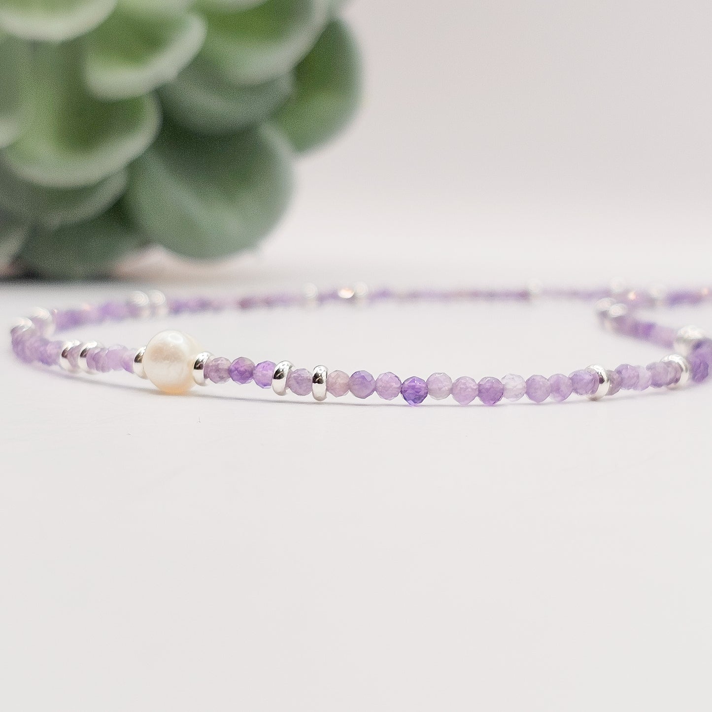 Side flat angle view of Amethyst pearl necklace laid down.