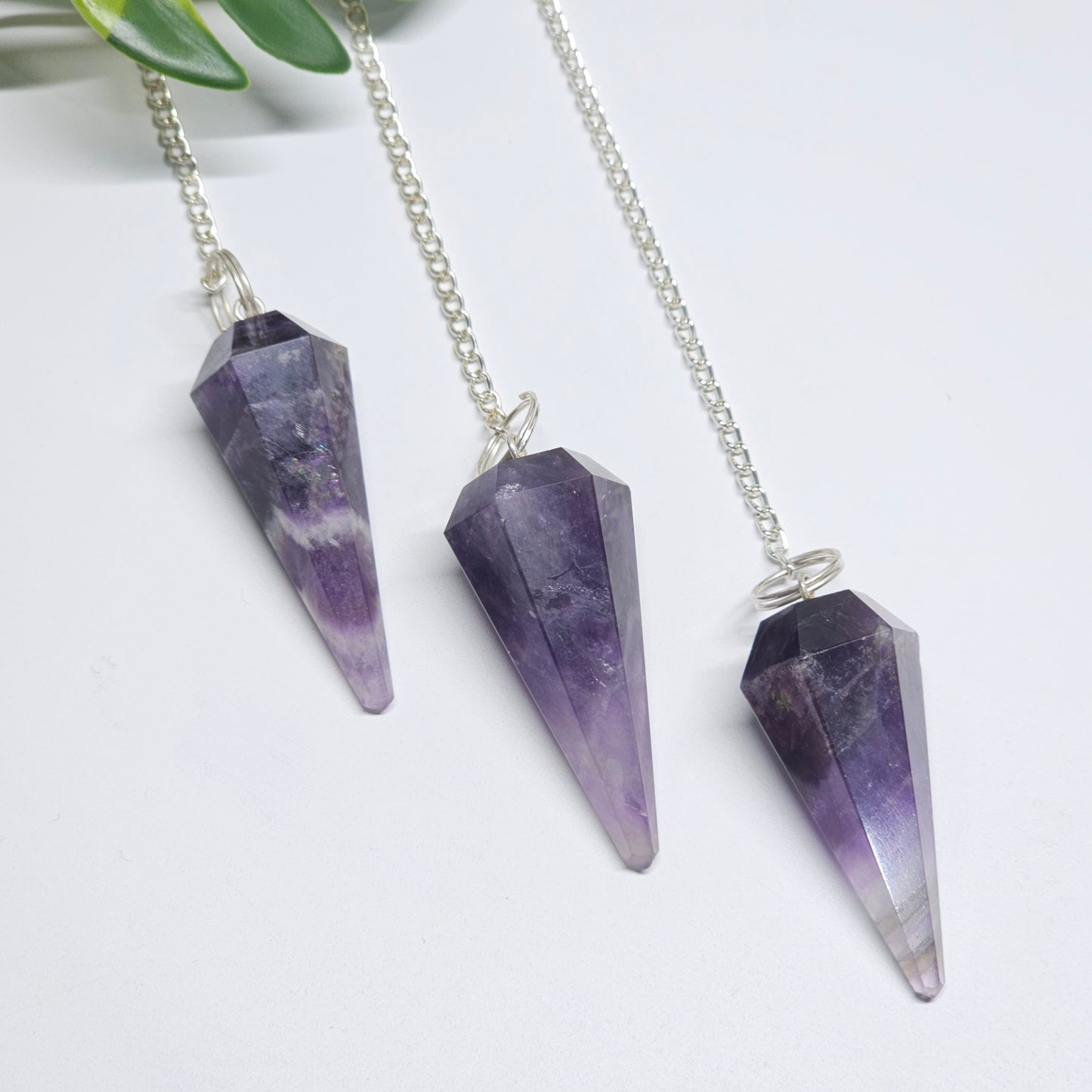 Polished Amethyst pendulums displayed on a flat surface, showcasing their natural clarity, pointed shape, and silver-tone chains.