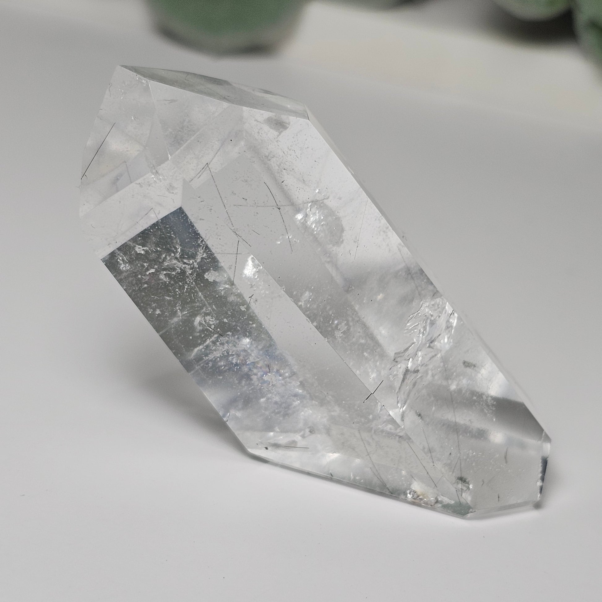 Black Rutile Quartz crystal tower displayed on a flat surface, showcasing its clear quartz body, fine sparse rutile inclusions, natural key formation, and polished angled formation.