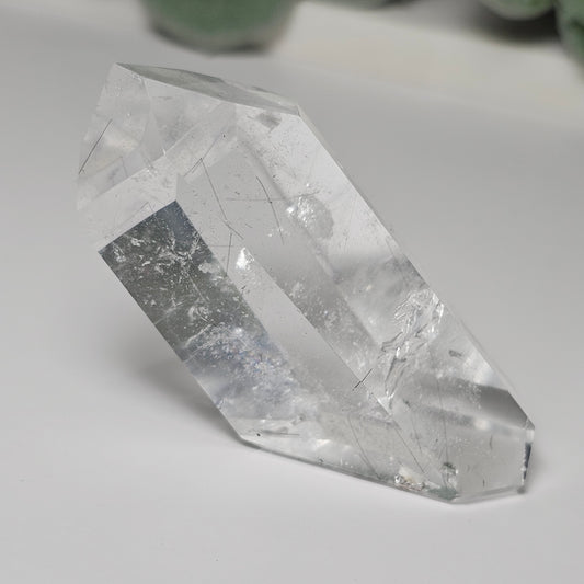 Black Rutile Quartz crystal tower displayed on a flat surface, showcasing its clear quartz body, fine sparse rutile inclusions, natural key formation, and polished angled formation.
