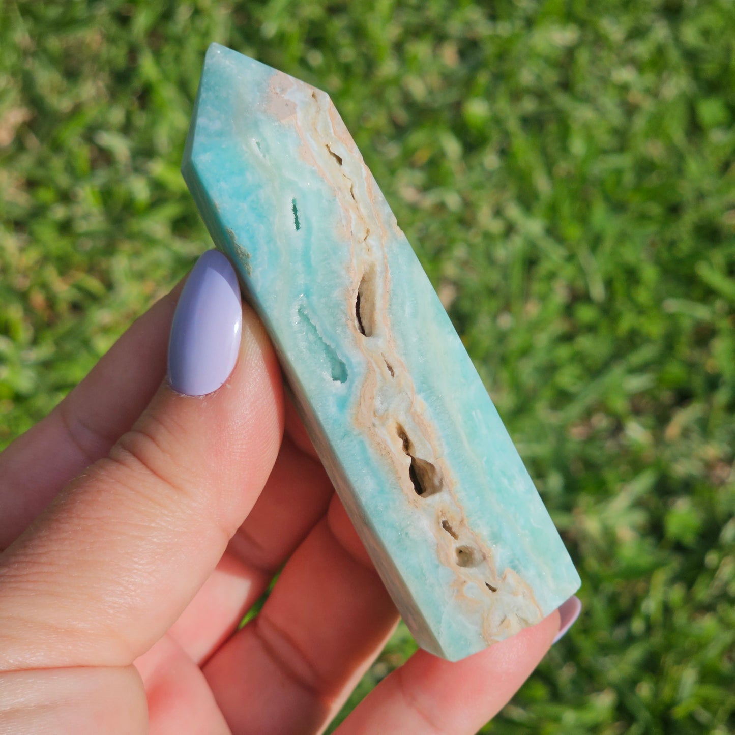 Blue Aragonite tower in natural sunlight held in hand to show size, natural pockets, and druzy features.