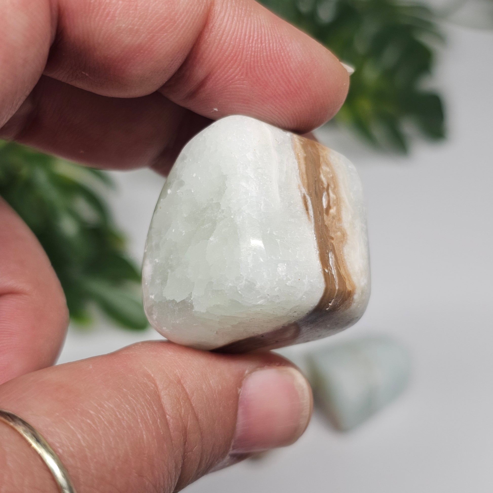 A medium Caribbean Calcite tumble stone held in hand, showcasing its size, natural banding, and polished finish.