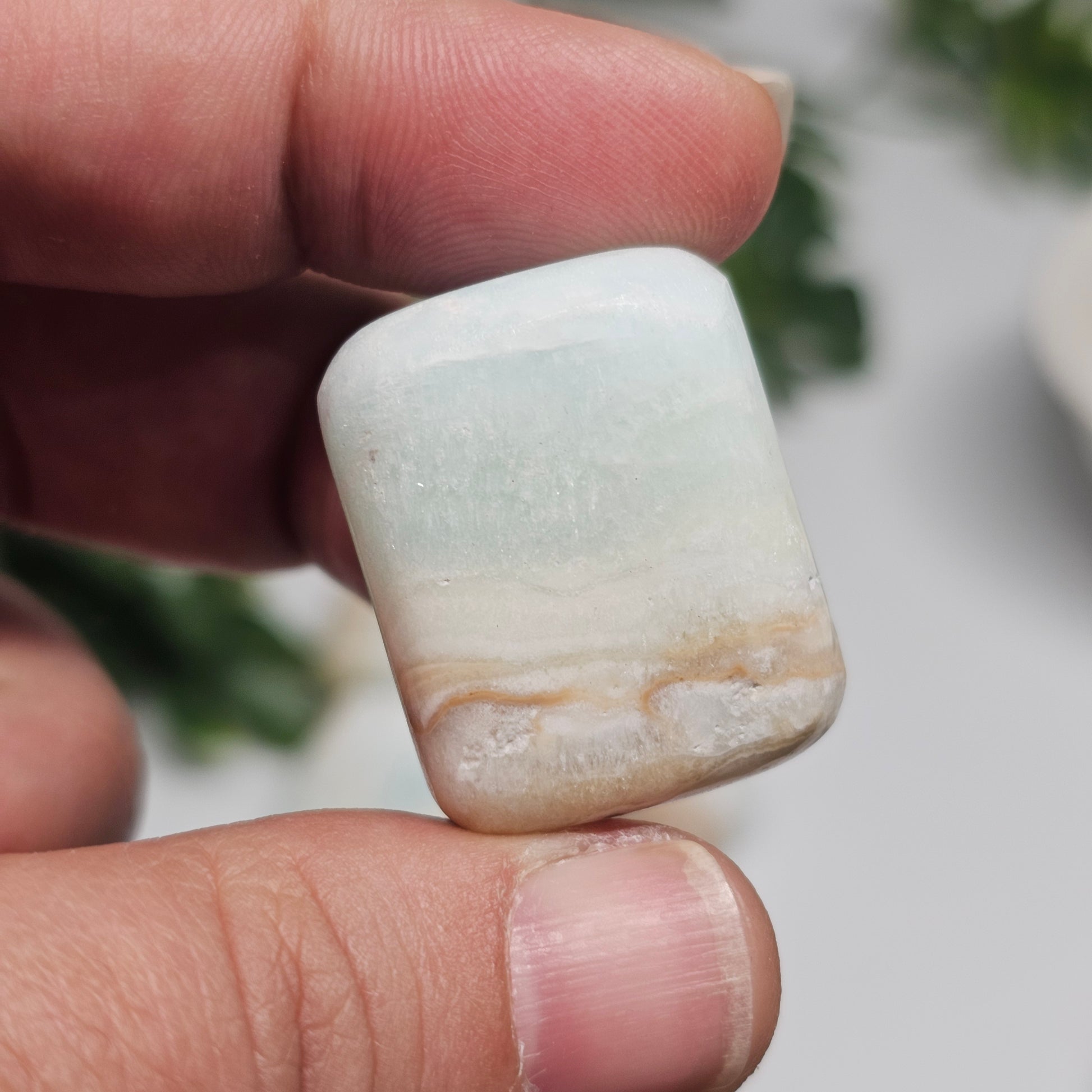 A small Caribbean Calcite tumble stone held in hand, showing its size reference, smooth polish, and calming blue tones.