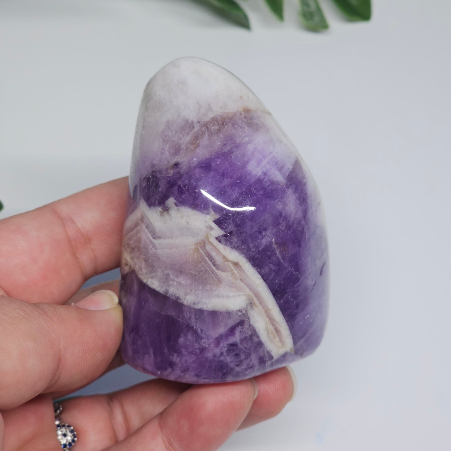 Chevron Amethyst polished freeform photographed in hand to show size, natural banding, and rich purple colouring with white Quartz patterns.
