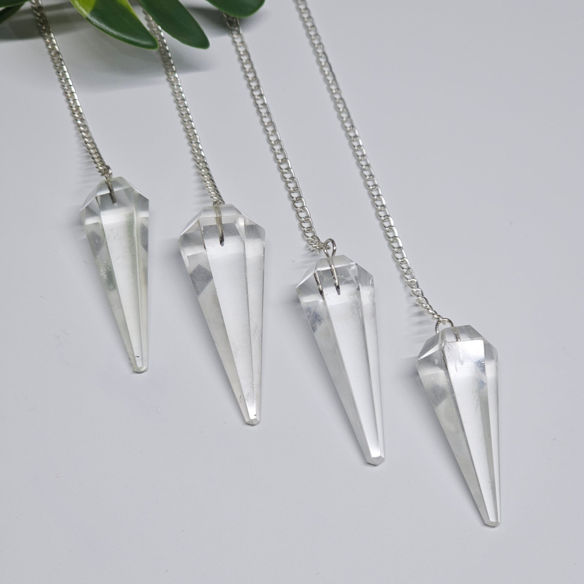 Polished Clear Quartz pendulums displayed on a flat surface, showcasing their natural clarity, pointed shape, and silver-tone chains.