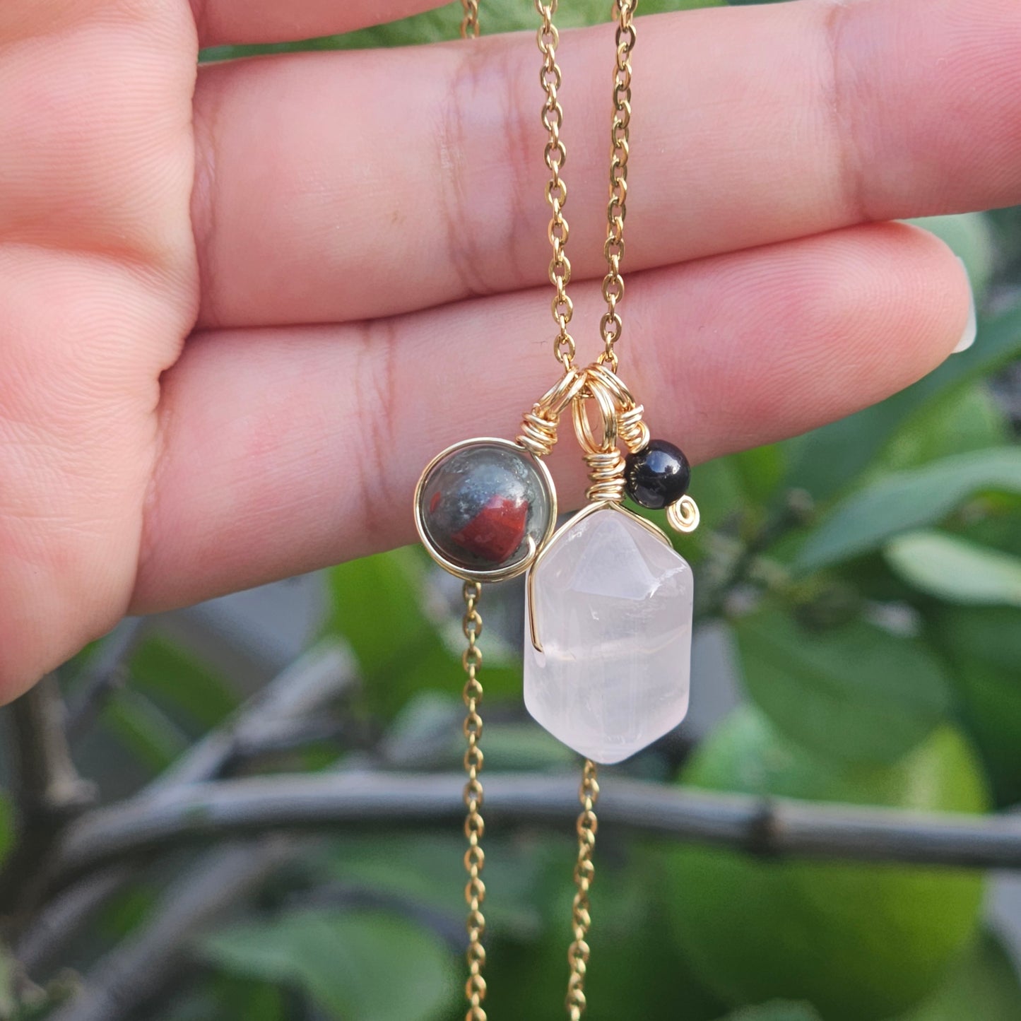 Close up of the Grounded Love crystal necklace hanging from a hand highlighting the Rose Quartz point Bloodstone Jasper and Black Tourmaline gemstone combination