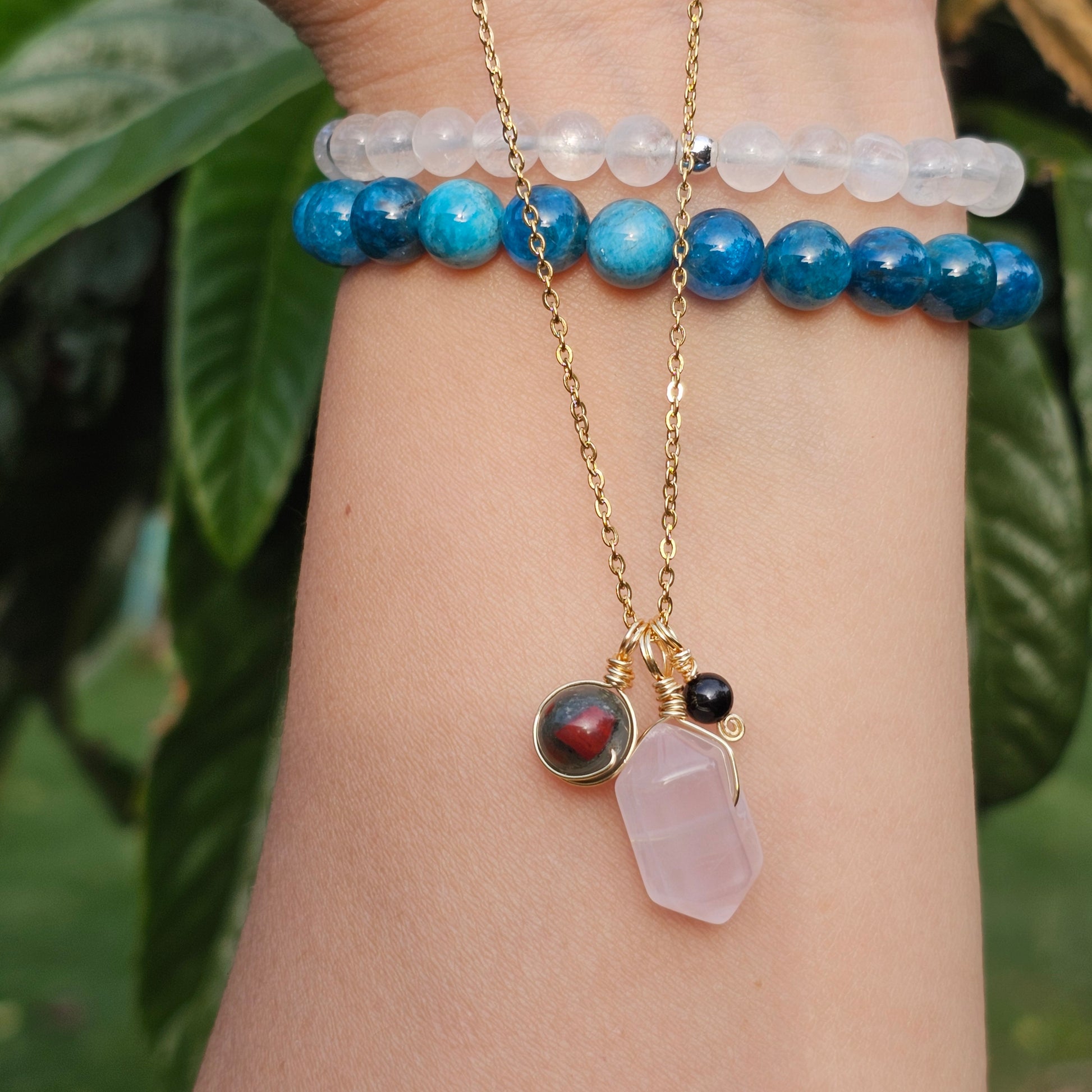 Grounded Love gemstone necklace draped over a wrist to show pendant size and details featuring Rose Quartz Bloodstone Jasper and Black Tourmaline on an 18k gold plated stainless steel chain
