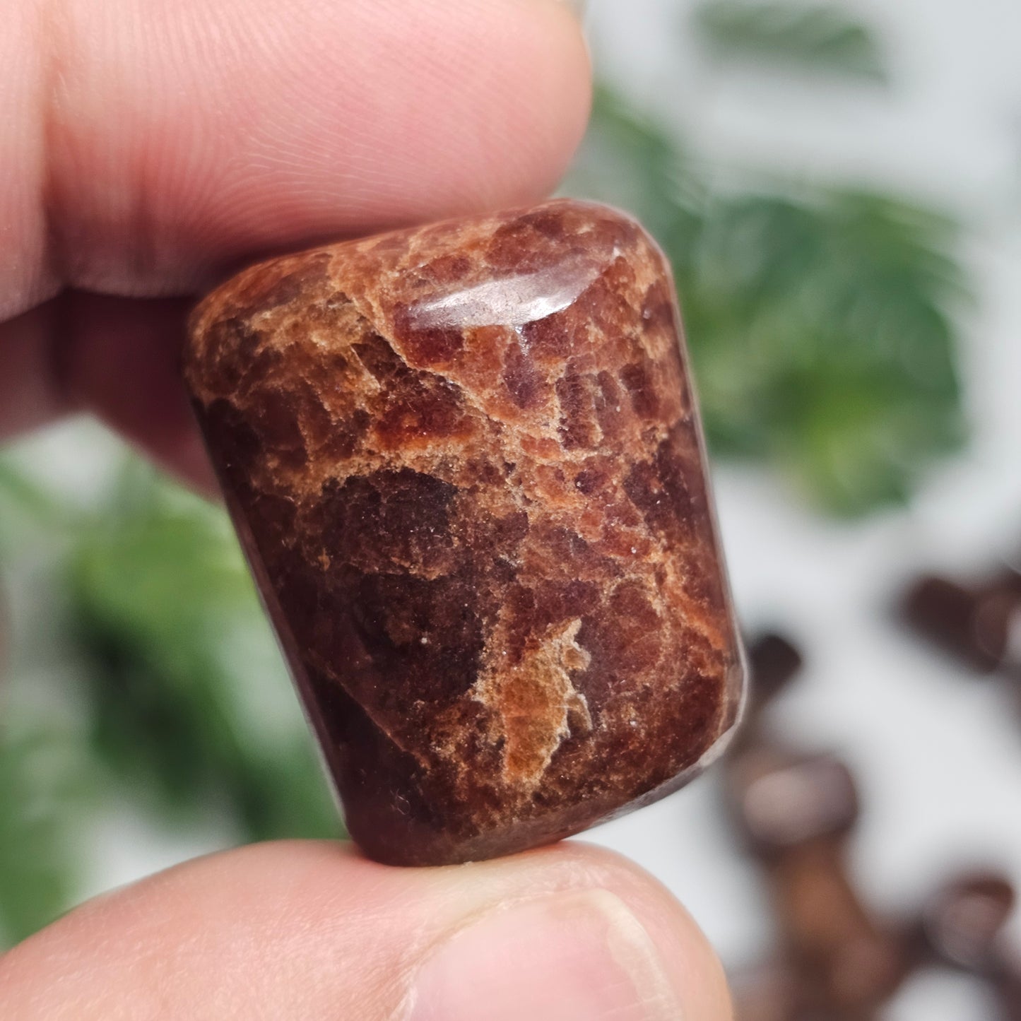 Close-up of a Hessonite Garnet tumble stone in hand, highlighting its smooth finish and distinctive natural characteristics.