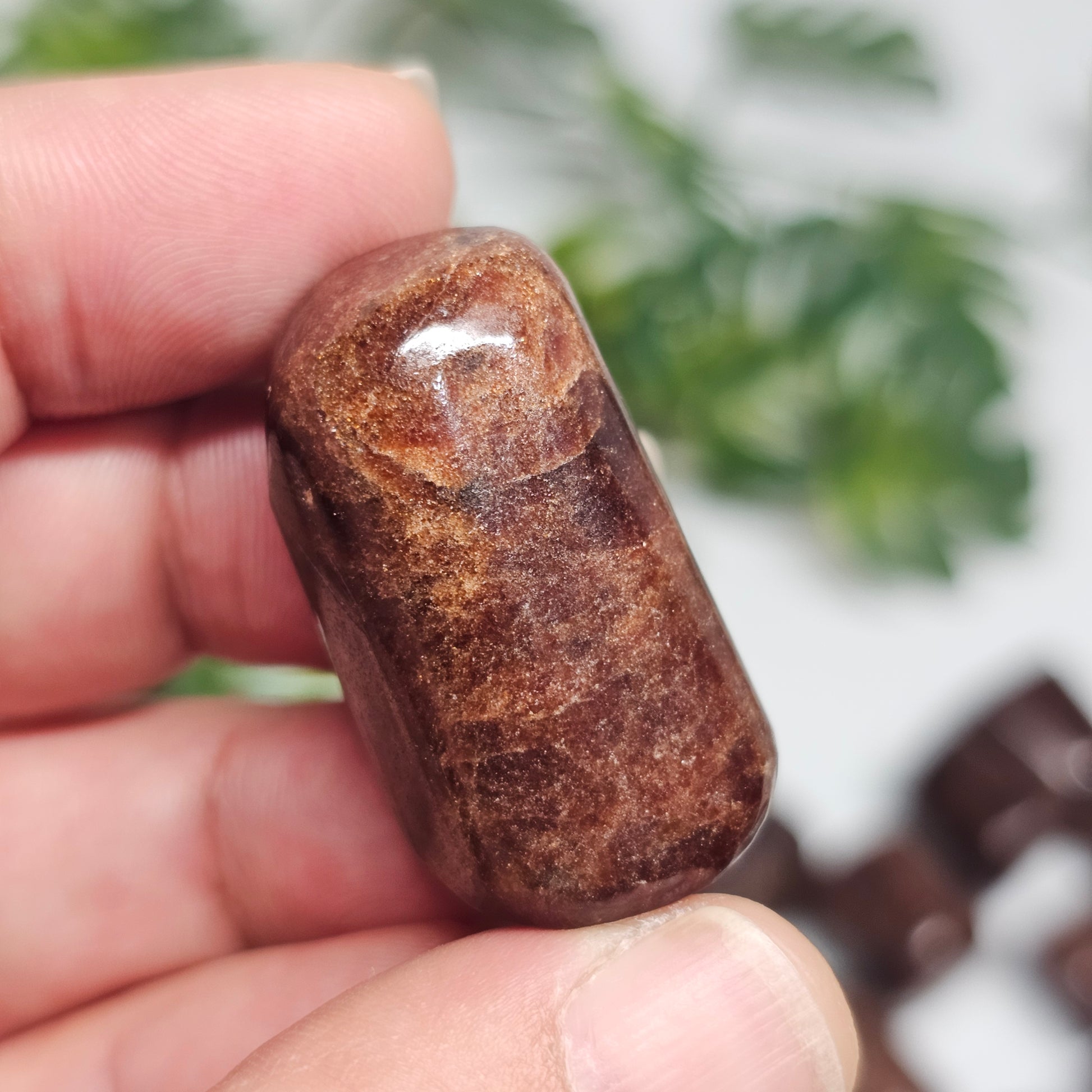 Handheld view of an individual Hessonite Garnet tumble stone, displaying its polished appearance and one-of-a-kind natural formation.