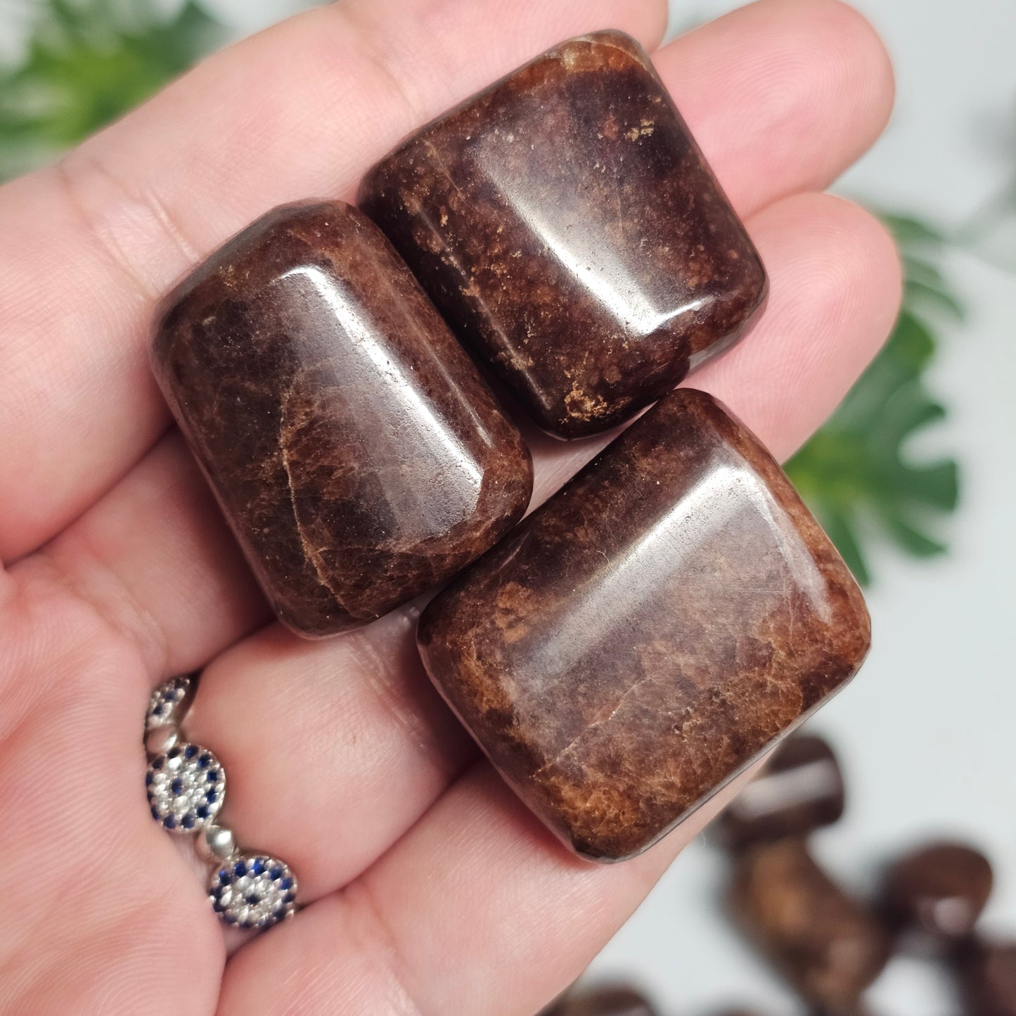 Multiple Hessonite Garnet tumble stones held in hand for size reference, displaying a variety of natural formations and polished finishes.