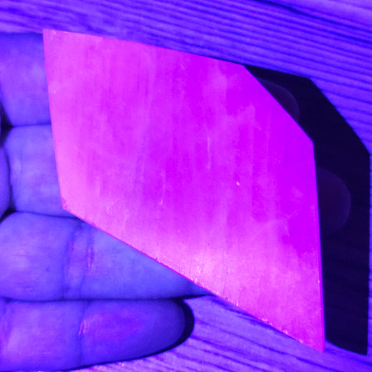 Kunzite slab under UV light showing fluorescence and internal glow, highlighting its natural crystal response.