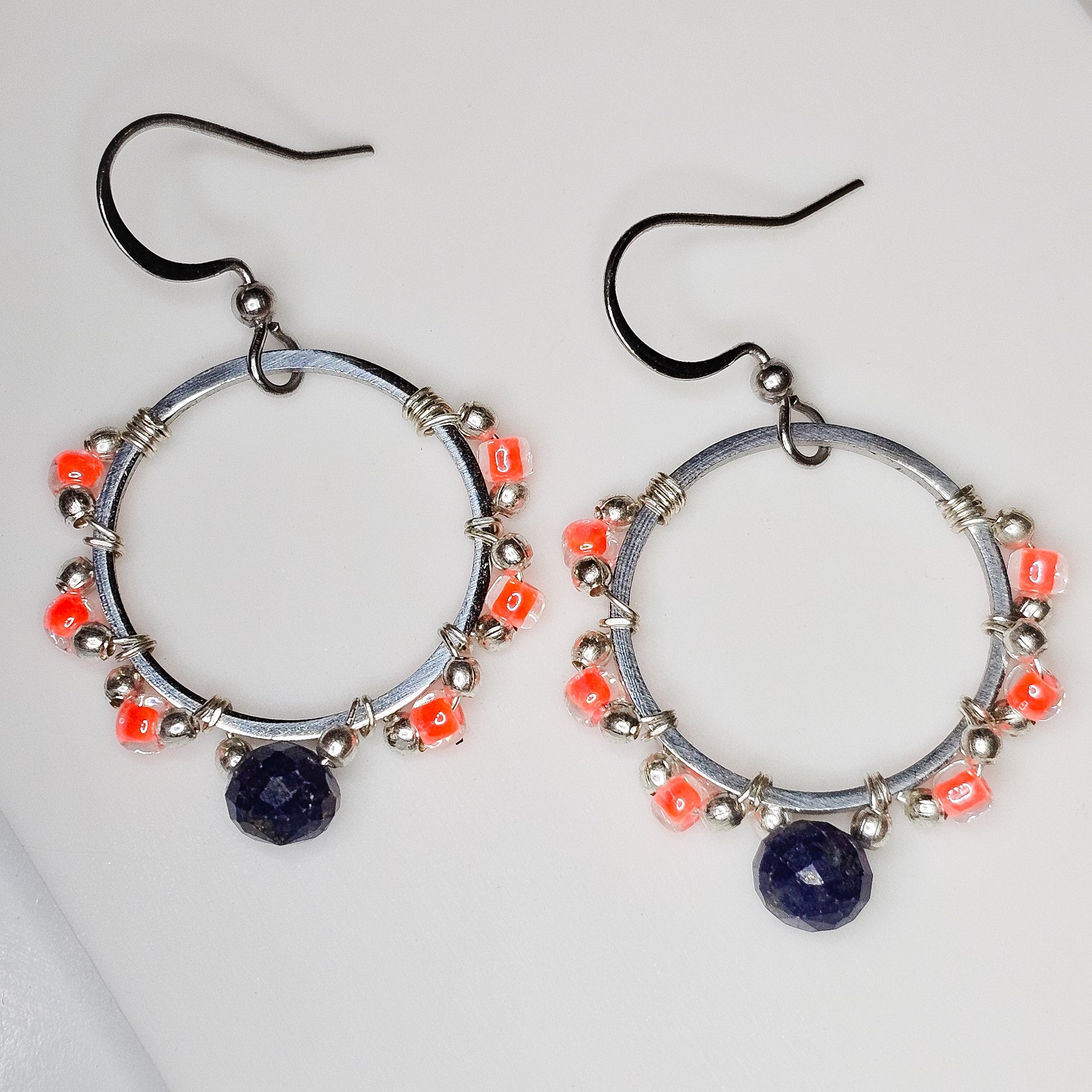 Full view of the handcrafted hoop earrings featuring Lapis Lazuli, neon orange Japanese seed beads, and silver accents suspended from stainless steel ear wires.