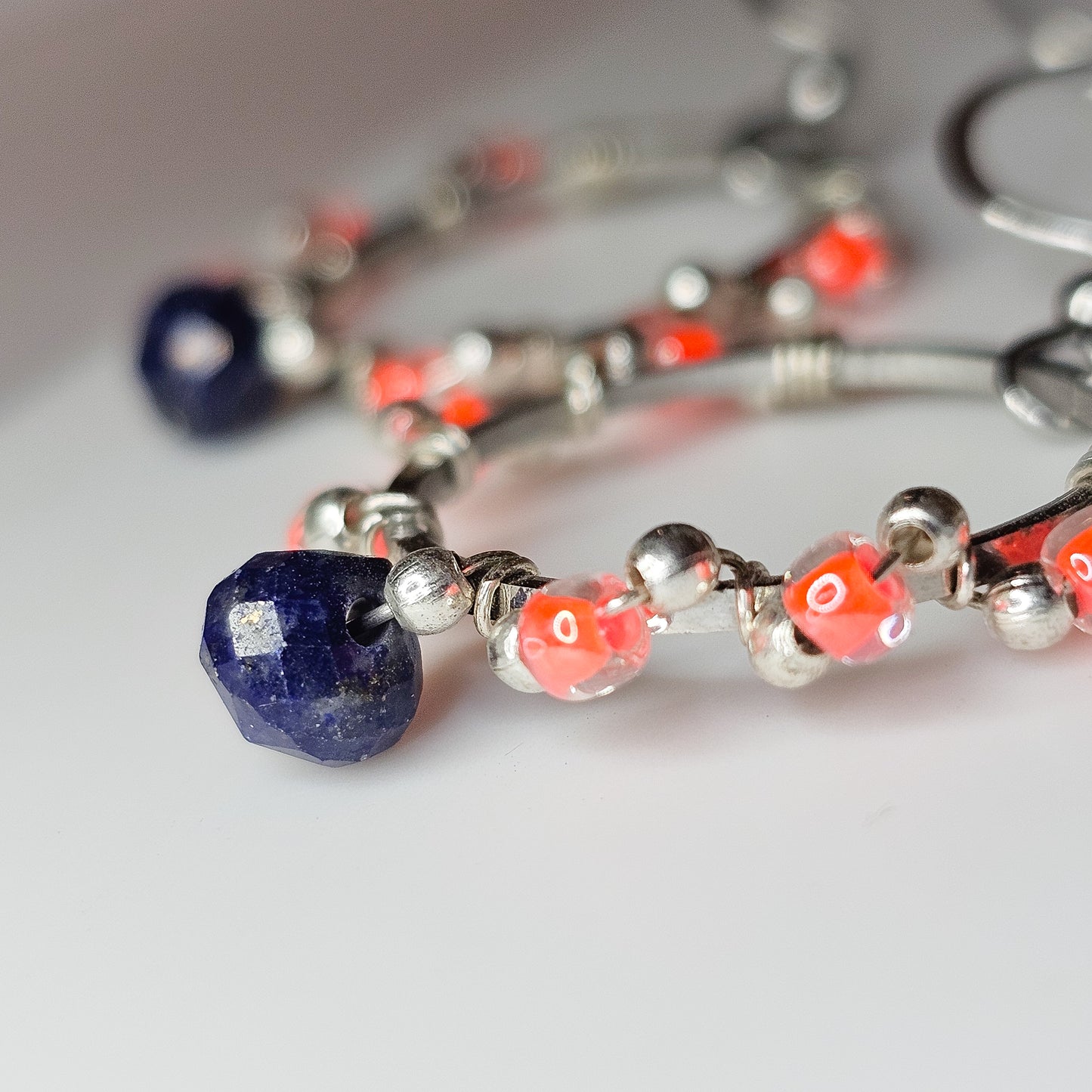 Close-up detail highlighting the deep blue Lapis Lazuli, vibrant neon orange seed beads, and mini silver bead wire wrapping on stainless steel hoops.